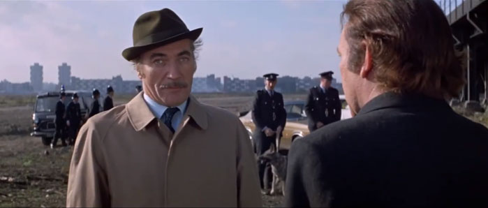 Richard Burton confronts a Scotland Yard detective on wasteland with tower blocks in the distance.