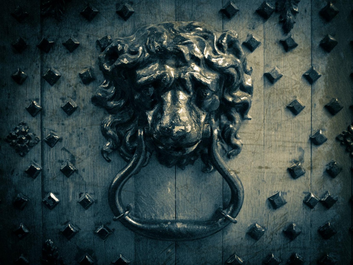 What looks like a still from a silent film of a door knocker in the shape of a lion's head on a castle door.
